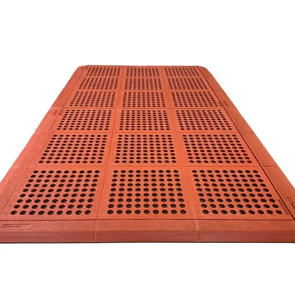 The Interlocking Catering Mat is a large red rectangular rubber mat with a grid pattern and round holes in each square for drainage and slip resistance, shown on a white background.