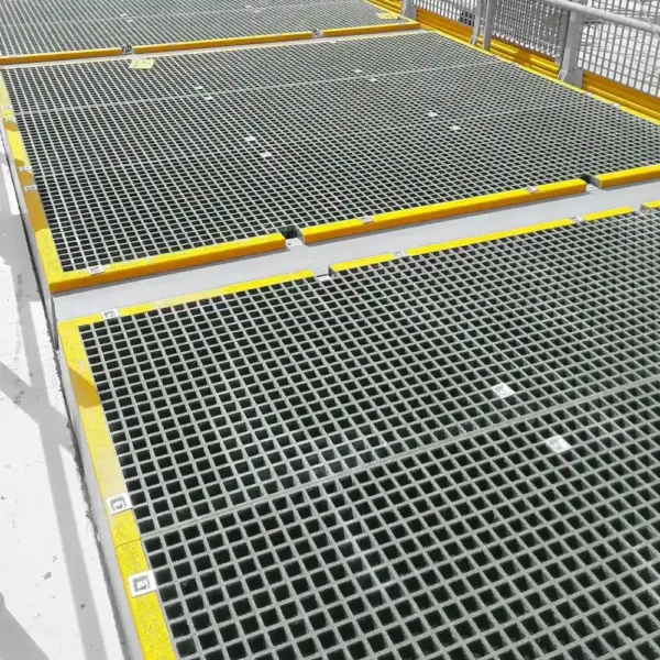 Open Top Grating panels with square openings and yellow-bordered edges create a clean, industrial walkway. A metal safety railing runs along the right side for protection.