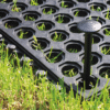 Close-up of an Interlocking Anti-Fatigue Mat with a black fixing peg securing it on grass. The mat features hexagonal openings, allowing green grass to show through.