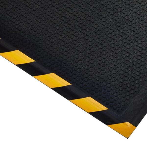 The Foam Cushioned Industrial Mat is a black rubber safety mat with a textured surface and a yellow-black striped border, pictured from a diagonal angle.