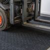 A close-up of a forklift’s front section with its forks resting on the Forklift Mat, highlighting the tyre and metal parts in detail.