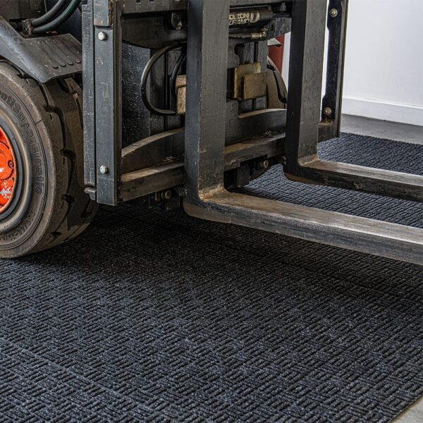 A close-up of a forklift’s front section with its forks resting on the Forklift Mat, highlighting the tyre and metal parts in detail.