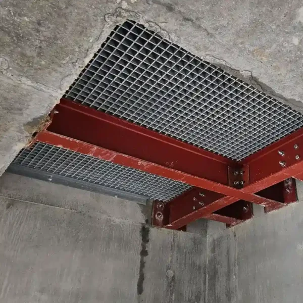 An Angle Profile is installed in a concrete ceiling, supported by red steel beams in a cross pattern. The surrounding concrete displays rough edges where the Angle Profile was fitted.