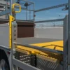 Close-up of a flatbed lorry featuring metal railings, safety barriers, and an Anti-Slip Flat Sheet yellow step platform, parked by a barbed wire fence under a clear blue sky.