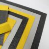 Several Anti-Slip Sheets in black, grey, and yellow, each featuring a textured rectangular design, are stacked with aligned corners to create a stepped, layered effect on a white background.