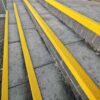 Outdoor concrete steps with Anti-Slip Stair Nosing in long, bright yellow strips for enhanced visibility and safety, bordered by low brick walls.