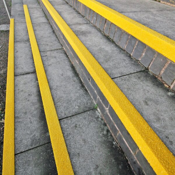 Outdoor concrete steps with Anti-Slip Stair Nosing in long, bright yellow strips for enhanced visibility and safety, bordered by low brick walls.