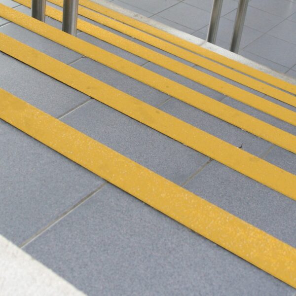 Anti-Slip Stair Nosing in grey with bright yellow safety strips improves step visibility and prevents slipping. Stainless steel railings are installed at the top.