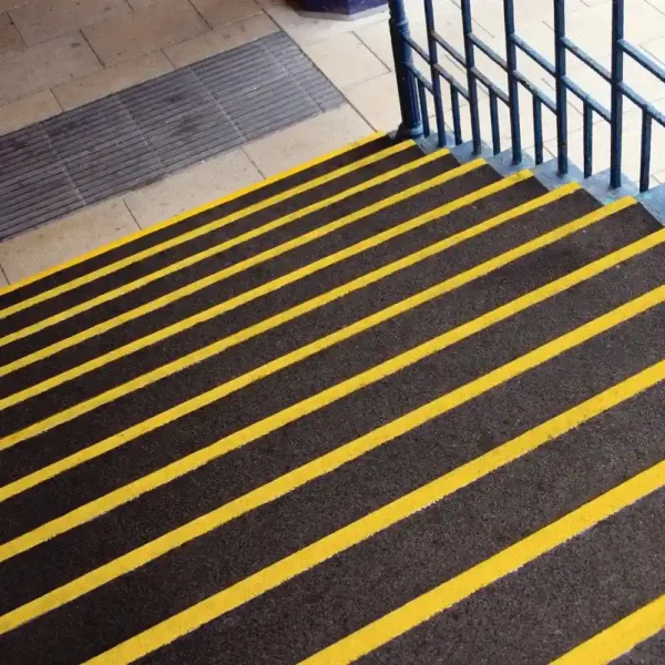 Dark brown stairs feature Anti-Slip Stair Tread with bright yellow safety strips on each edge, adjacent to a blue metal handrail and beige tiled upper floor.