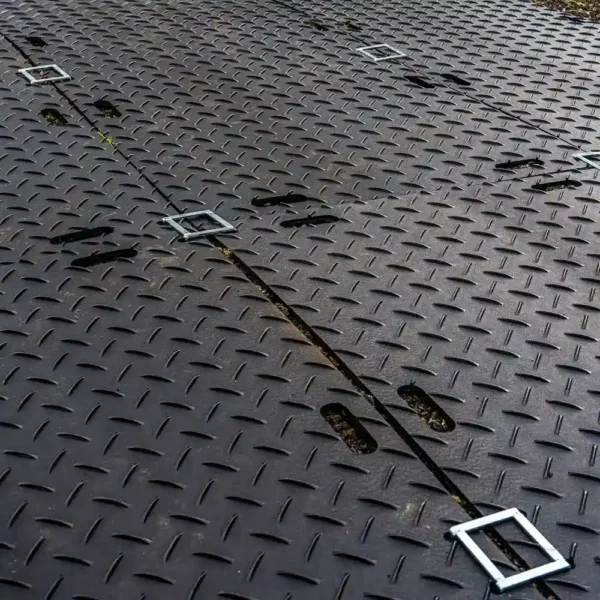 Close-up of the Heavy-Duty Ground Protection Mat’s dark metal surface, showing a chequer plate pattern with rectangular handles and elongated slots arranged in parallel rows.
