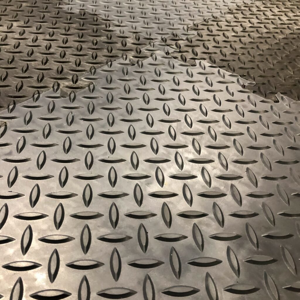 Close-up of a Chequer Plate Interlocking Tile floor, with a wet, reflective section in the foreground contrasting with the drier, matt area in the background.