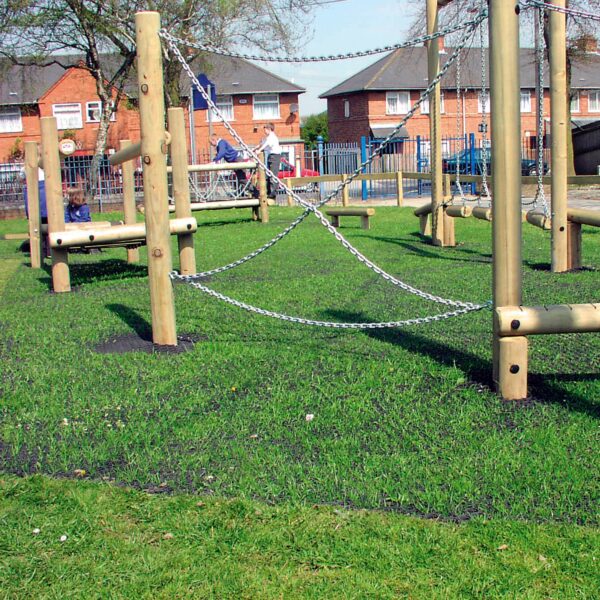 A Grass Mat Roll (1m x 10m x 22mm) is installed beneath wooden playground climbing equipment with chains and ropes on a sunny park lawn, with houses and trees visible in the background.
