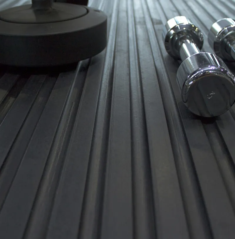 Close-up of a black ribbed gym floor mat with two chrome dumb-bells and the base of a larger weight resting on it.
